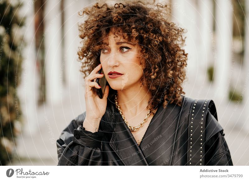 Retro businesswoman talking on smartphone in park walk speak retro path commute outfit style female old fashioned 80s cool leather jacket lifestyle road street