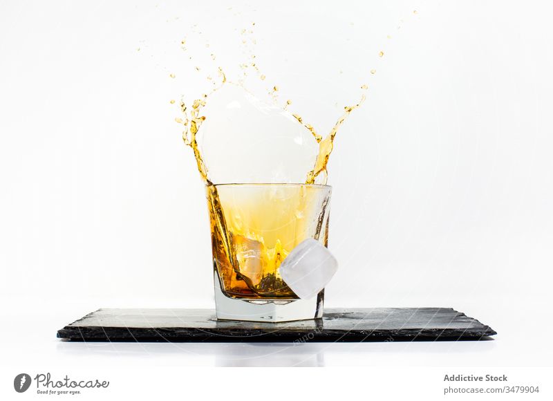 Ice cubes falling into glass with drink ice splash yellow cold liquid beverage slate fresh refreshment moment transparent alcohol cocktail whiskey crystal board