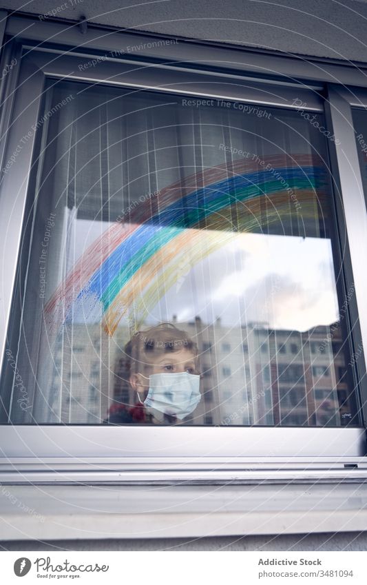 Boy behind window during quarantine boy mask medical rainbow colorful home hospital frown pandemic coronavirus covid 19 child kid childhood sad unhappy hygiene