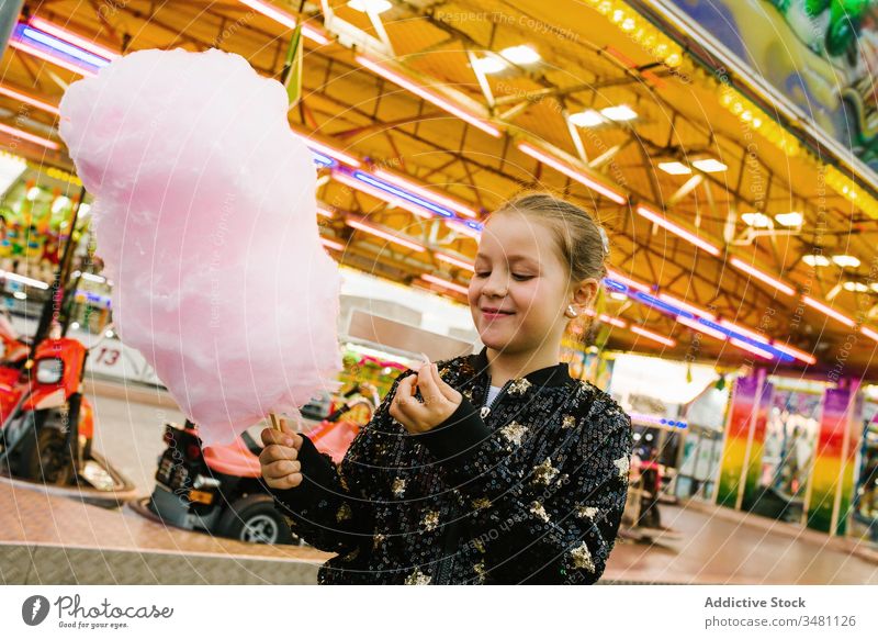 Girl eating cotton candy on funfair girl candyfloss smile lights city entertainment kid happy child urban sweet delighted treat lifestyle cheerful little sugar
