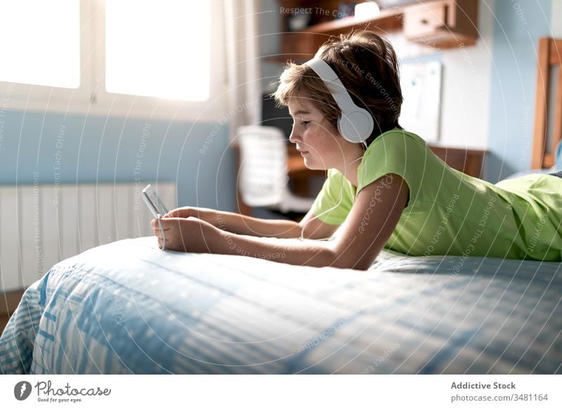 Cheerful kid watching movie on tablet in bedroom gadget home headphones cheerful boy using laugh child online listen internet happy lifestyle device modern