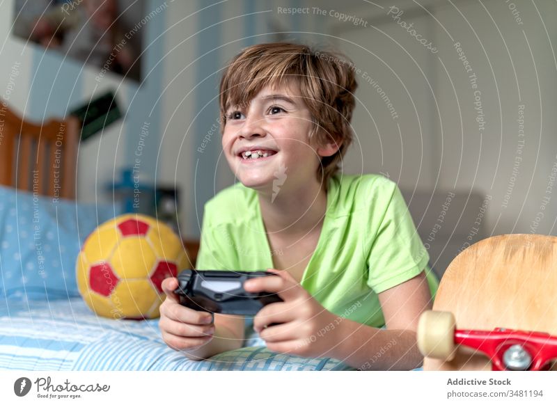 Happy boy playing video game in bedroom kid fun gamepad device excited gadget home lying cheerful using console child happy lifestyle modern connection digital