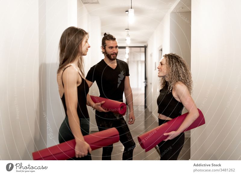 Young friends communicating in yoga class training studio standing talk mat ready together break sportswear man women workout fitness exercise activity club