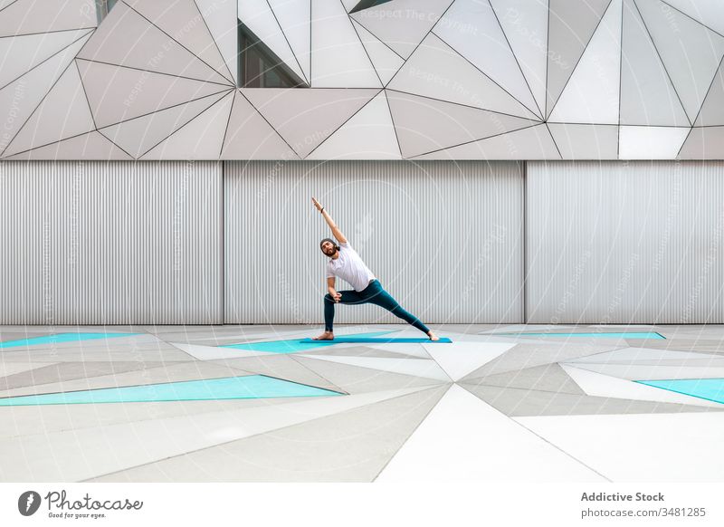 Man doing yoga exercise in geometric room man training geometry side angle pose modern stretch fitness shape male sportswear architecture contemporary wall