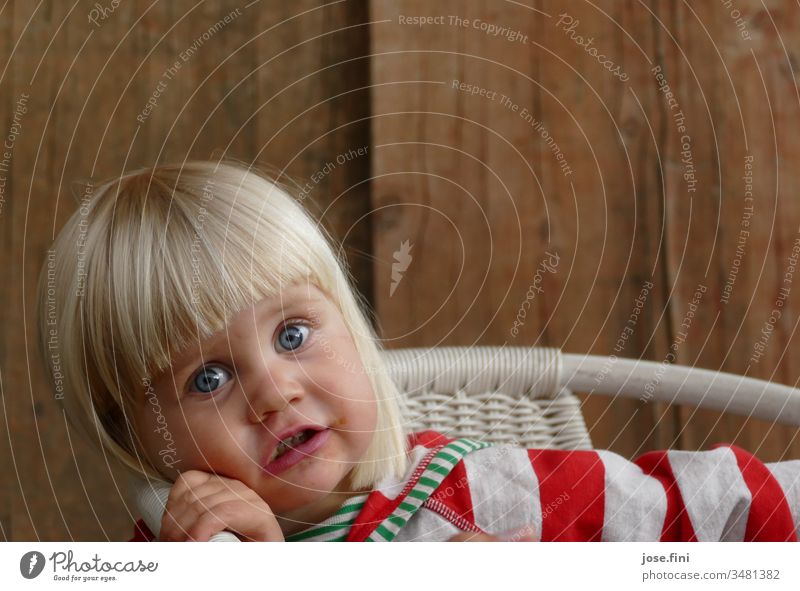 Little girl sits on a chair and looks into the camera with big eyes portrait Child little girl natural Brash Cute excited listen understand spellbound Impish