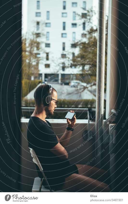 Man with headphones sits on the balcony in the evening sun and watches something on his smartphone, concept of staying home and social distancing Balcony Media