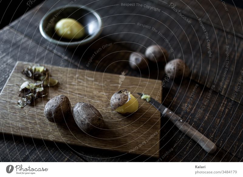 Boiled potatoes on wooden board with knife Potatoes in their jackets peel salubriously peeled shell Wooden board boil still life layflat Knives Old pellen