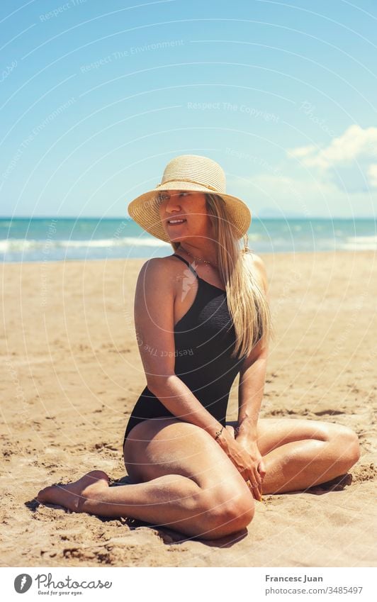A woman with a beautiful body and a big breasts on the beach. Model posing  on the beach in a swimsuit. Young blonde girl sunbathing on the beach near  the rock. Stock