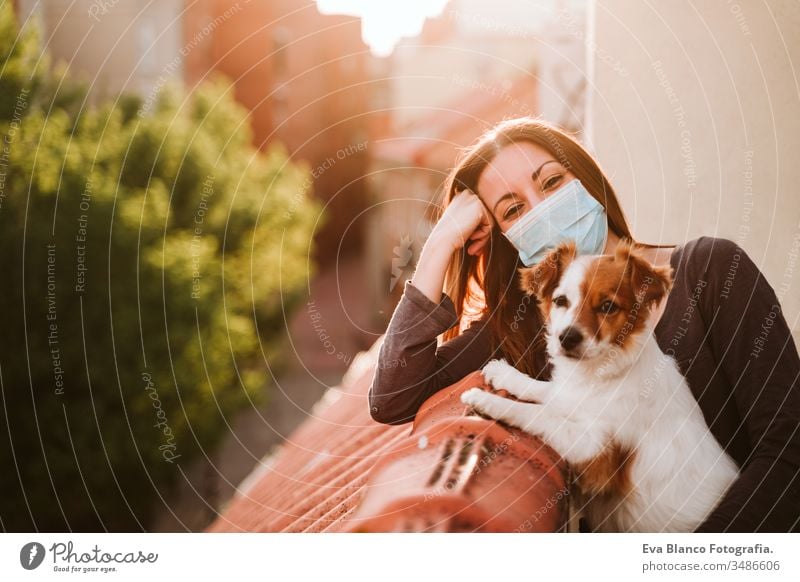young woman at home on a terrace wearing protective mask. Hugging her cute jack russell dog. Corona virus Covid-19 concept pet coronavirus covid-19 indoors