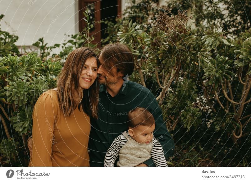 Lovely couple standing together while man holds their baby son alternative indie hipster smile woman dad parents portrait outdoors garden lifestyles wife