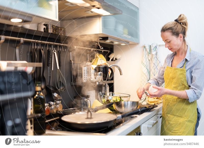 Stay at home housewife woman cooking in kitchen, salting dish in a saucepan, preparing food for family dinner. young healthy meal person vegetable female