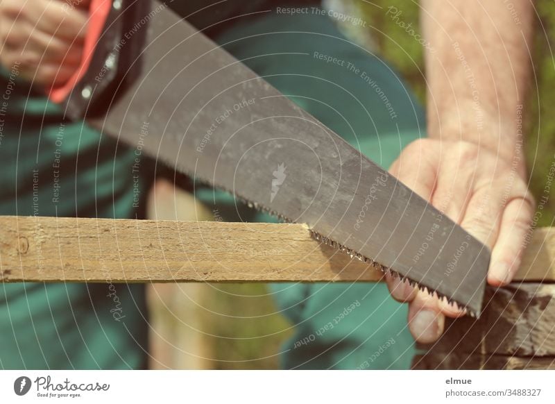 Man saws through a wooden slat with a foxtail - cutout Jacksaw Saw Tool Occupational health and safety Craftsperson to it yourself Hand Wood latte Craft (trade)