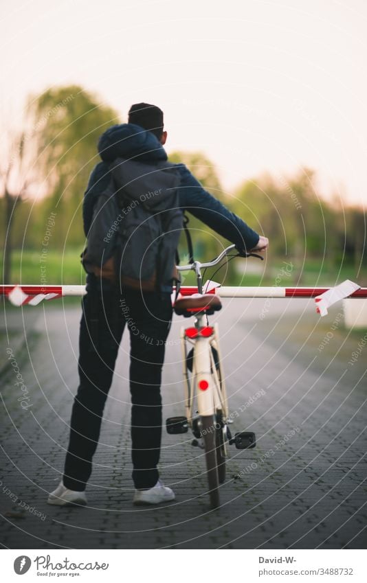 Man stands with his bicycle in front of a locked barrier. too cordoned off Bicycle Stand Wait interdiction Anonymous Rear view completed forbidden Safety