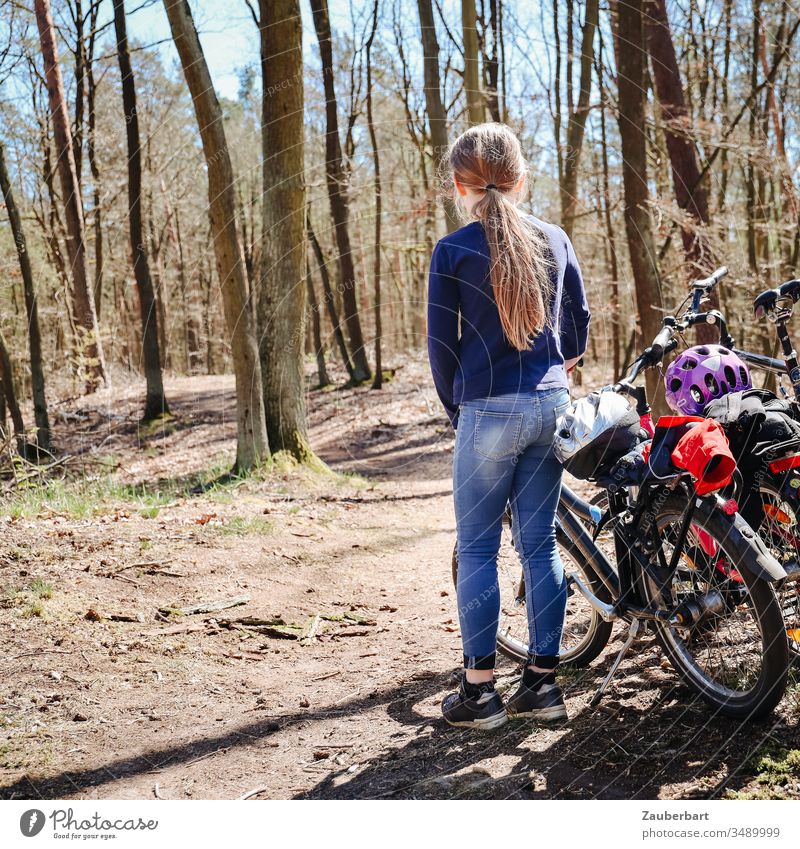 Child with bicycle stands on a forest path during a bicycle tour Girl Bicycle bike tour Forest trees jeans Ponytail Sun Infancy Family