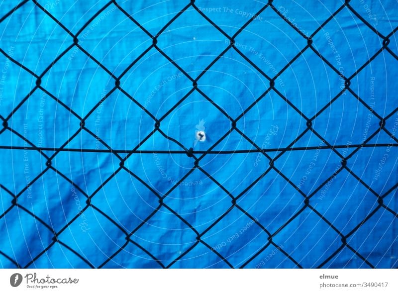 Mesh wire fence in front of blue PVC tarpaulin with small hole Wire netting fence Screening Protection demarcation Hollow Peephole Fence Boundary Border Blue