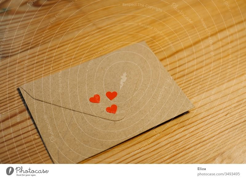 An envelope with three little red hearts on a brown wooden table; concept love, love letter Envelope (Mail) Letter (Mail) Love letter cuddle Greetings Heart Red