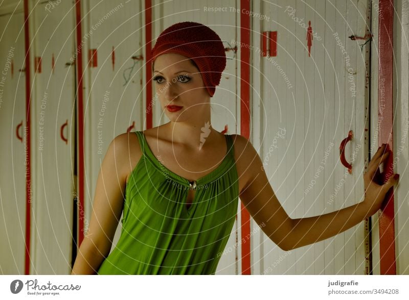 The girl with the beautiful red bathing cap and the green swimsuit is leaning elegantly against the door of the pool changing rooms. A summer love. Girl Woman
