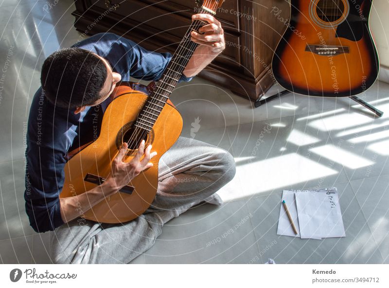Man playing guitar and composing music at home near a bright window on a sunny day. Casual musician sitting on the floor playing the guitar. man compose