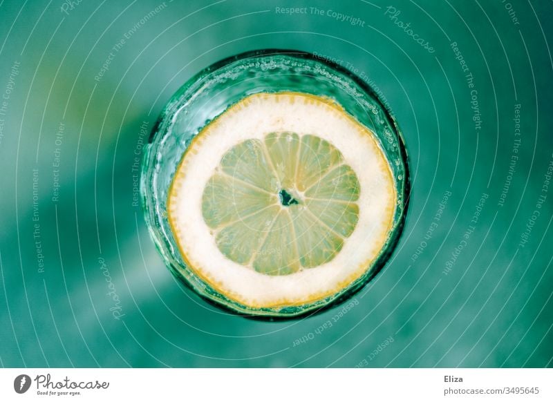 A glass of sparkling water with a slice of lemon from above on a turquoise green background Water Tumbler Slice of lemon Glass fizz fizzy Blur Round