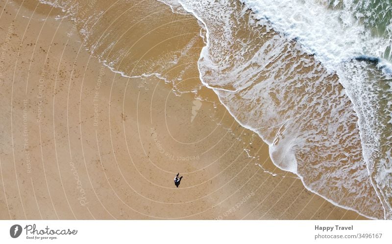 Aerial view of a sand beach. A man is sat on the sandy looking at the wave breaking close to him. Sunny day sunny day waves sea ocean orange loneliness