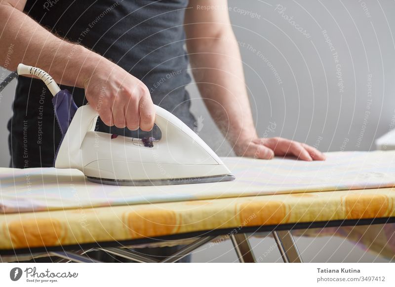Men's hands hold a white iron and iron on the ironing board. Close-up. Faceless. Copy space. Domestic duties are performed by men. lifestyle housework linen