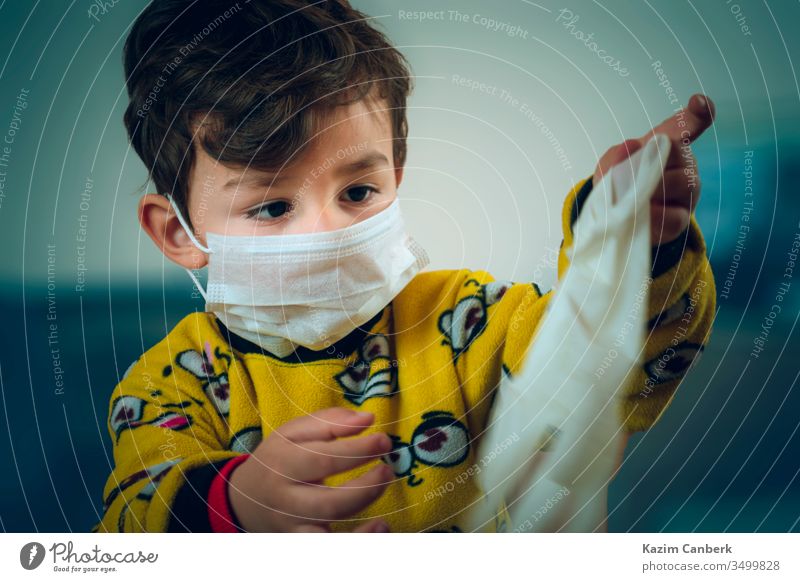 Happy looking 3 years old baby wearing pajamas and mask plays with surgical gloves kid corona virus global pandemic epidemic turkey turkish protection curfew