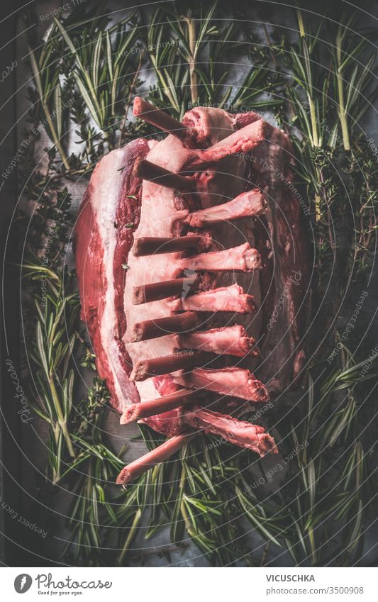 Close up of raw lamb racks. Dark rustic kitchen table with herbs und spices. Top view. Raw meat. Lamb crown roast making close up preparation dark background