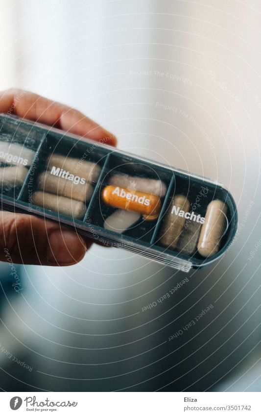A person holds a medicine box in which different tablets and pills are sorted for the different times of day drugs Nutrional supplement diverse Tin pill box