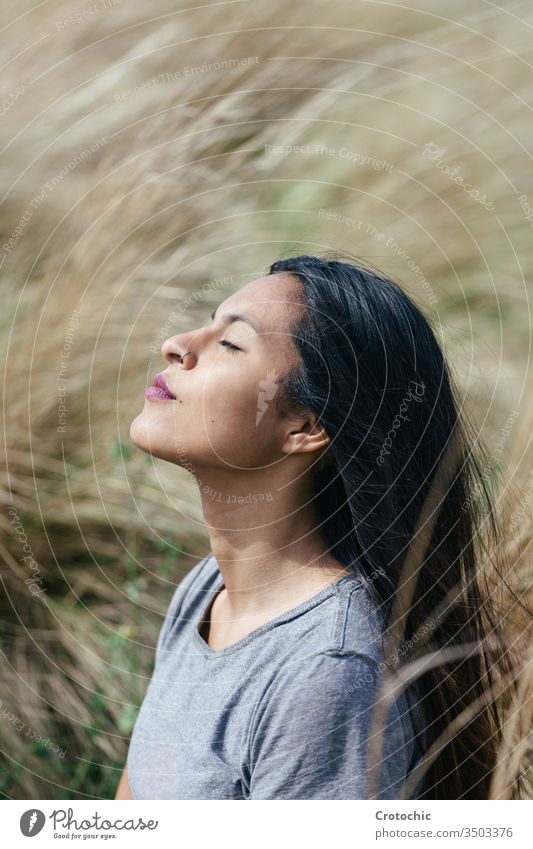 portrait of a young brunette woman with her eyes closed meditating vertical expression face profile dream raising sunlight female field nature comfortable