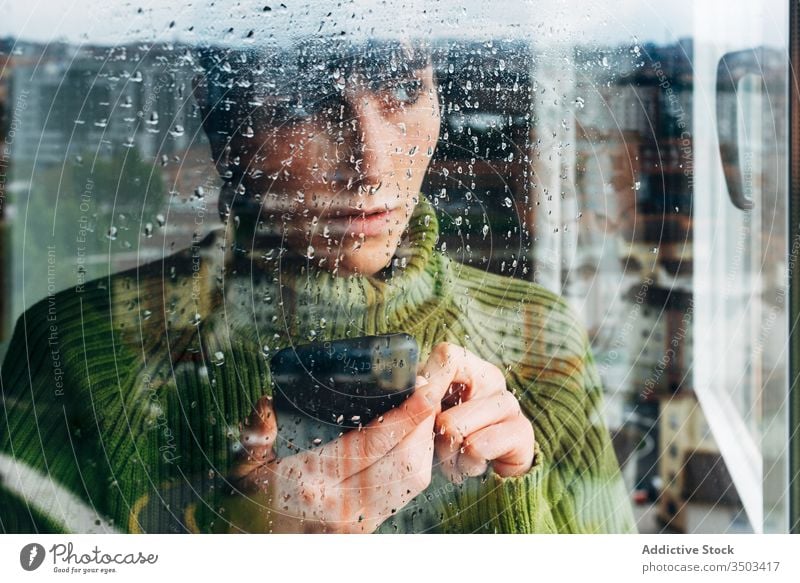 Young woman with smartphone standing near window home using lonely sad self isolation browsing gadget coronavirus covid-19 quarantine young female casual