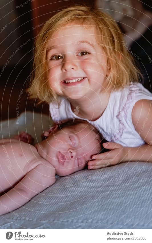 Happy small girl caressing with love newborn sleeping in soft bed at home kid sister infant calm relax innocent sibling rest little child interest friendly face