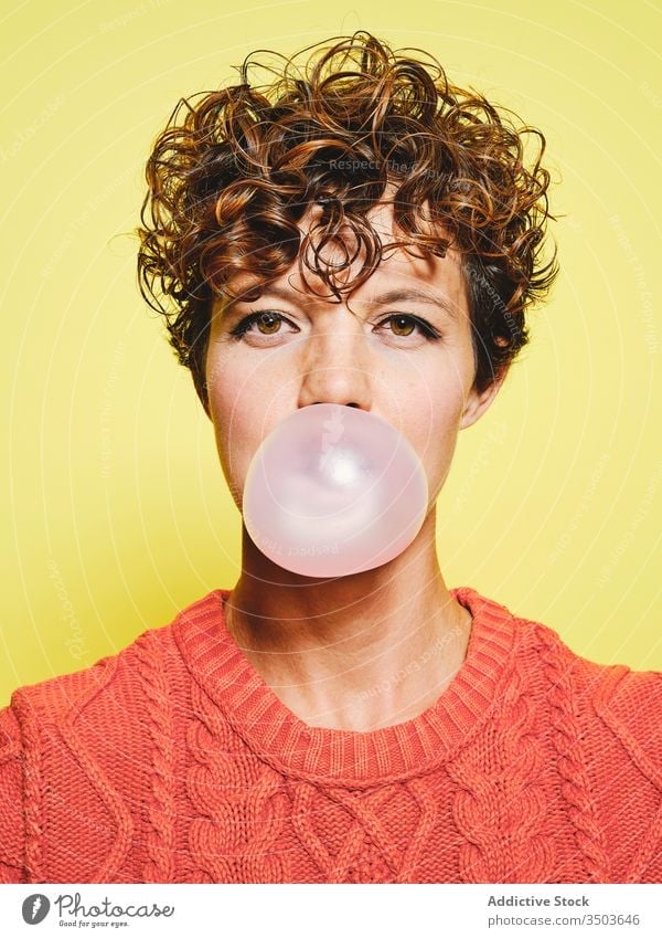 Funny young woman blowing bubble gum sweater orange casual style fun curly hair trendy bright female vivid vibrant expressive model colorful cool outfit modern