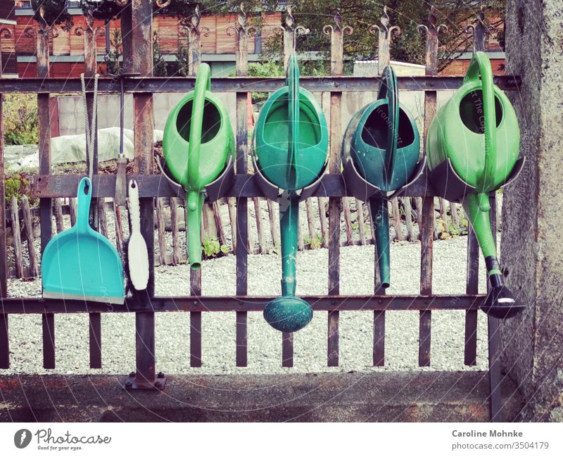 Four green watering cans and shovel with hand brush at the cemetery fence Shovel Fence Cemetery fence Green Colour photo Exterior shot Deserted Death Day Grief