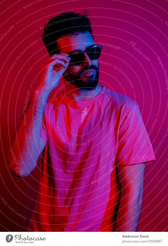 Serious bearded guy adjusting sunglasses man modern style serious red light bright outfit male trendy t shirt apparel confident garment illuminate neon