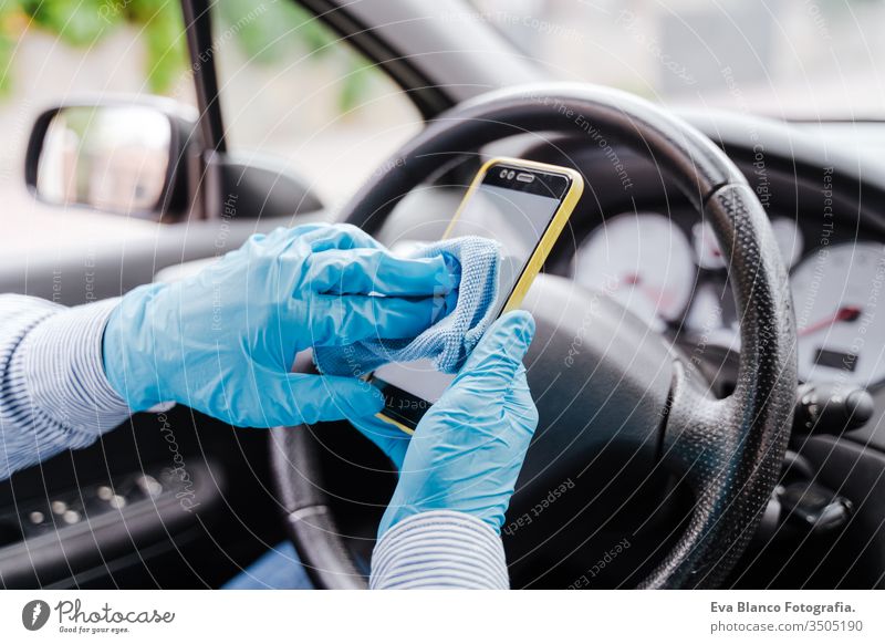 man disinfecting mobile phone with alcohol gel in a car wearing protective mask and gloves during pandemic coronacirus covid-19 driving protective gloves virus