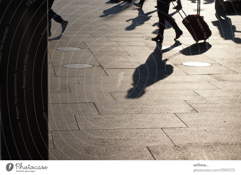 Travellers with long shadows and wheeled suitcases on the station square Shadow people trolley Suitcase Train station Going sunny Group go away