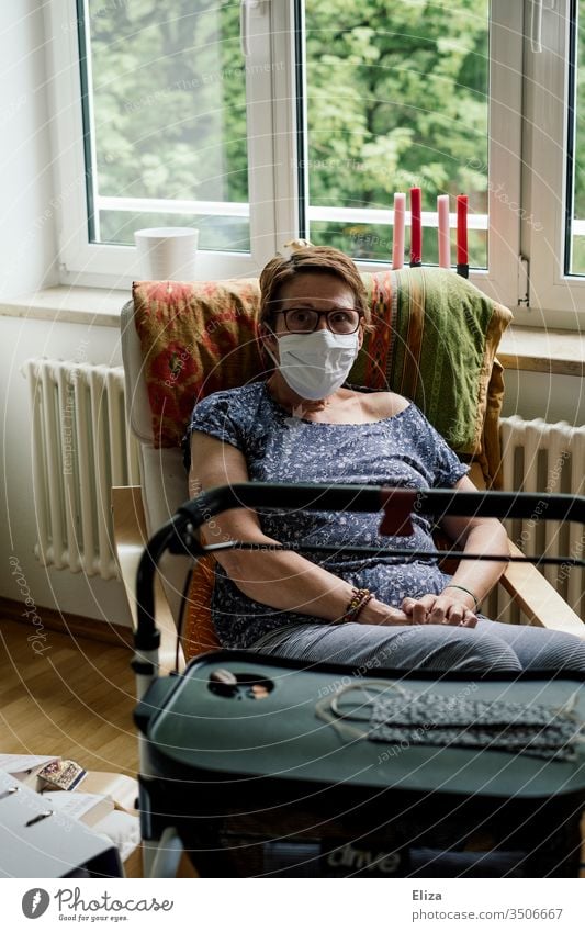 Woman in the risk group with mask and rollator sits alone at home in isolation due to the corona crisis Risk group covid-19 insulation Mask