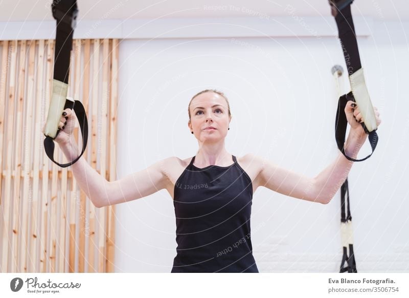 Young woman with battle ropes exercise in the fitness gym - a