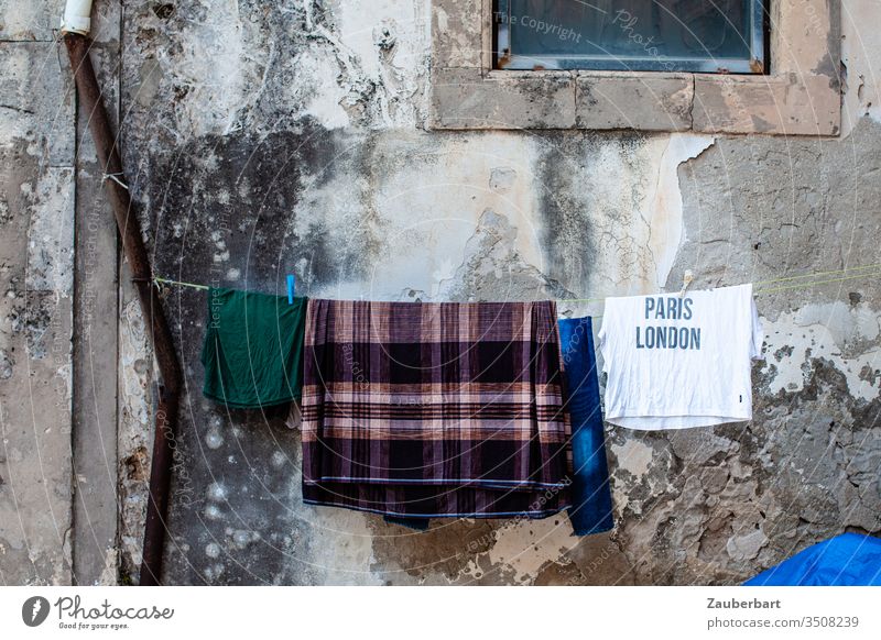 Longing - T-shirt with inscription Paris London hangs with other pieces of laundry on the line in front of an old wall in Sicily Wall (building) Clothesline