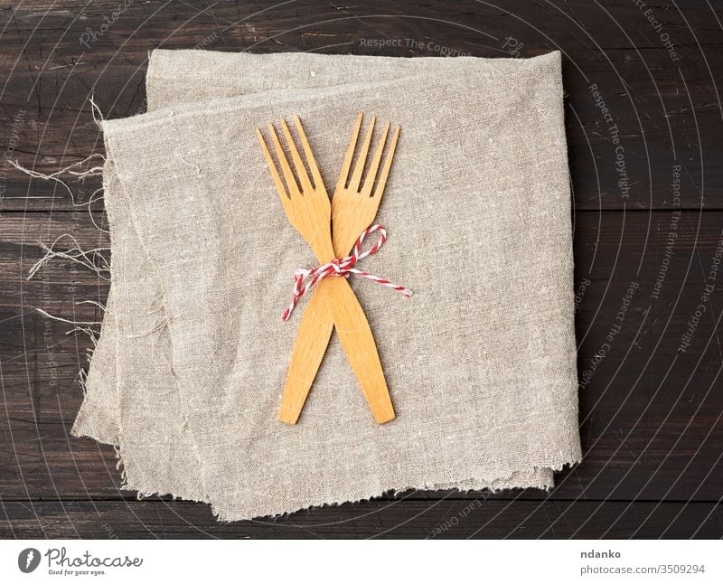 two wooden forks are tied with a rope and lie on a brown wooden background from boards homemade household kitchen kitchenware napkin gray linen blank clean
