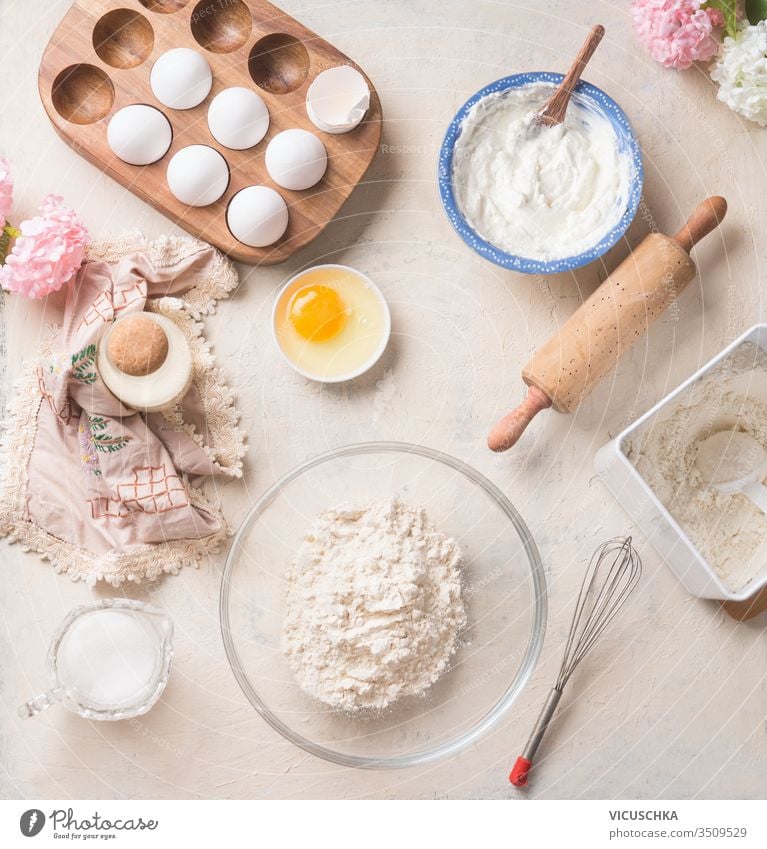 Modern baking background with flour in bowl, eggs and ingredients on white kitchen table background, top view. Home Bake. Recipes to cookies, pie and cake