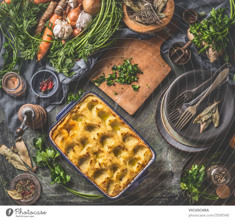 Baked mashed potato in casserole with spoon on dark rustic kitchen table background with ingredients and vintage utensils. Top view. Tasty home cuisine top view