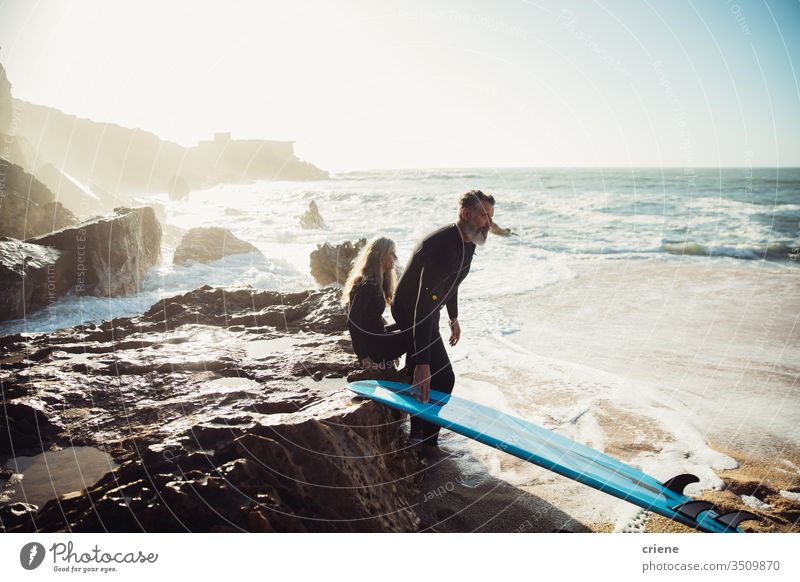 Senior couple sitting together on rocks with surfboards taking a break senior men vacation beach surfing adult beard grey hair lifestyle joy sport hobby