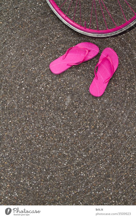 Bright pink flip-flops, standing abandoned on the asphalt of the road in summer, in front of a pink bicycle tire, waiting for their owner. Summer Flip-flops