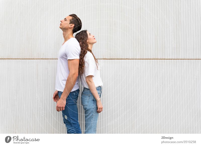 Young couple standing back to back against white urban wall woman young people female girl happy 2 portrait background beautiful casual attire caucasian guy