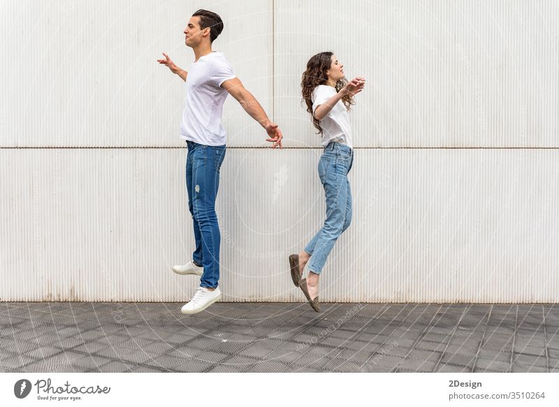Young couple jumping back to back against white urban wall lifestyle young caucasian woman happy city happiness beautiful girl fun two love summer female