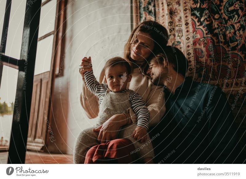 Lovely portrait of cute couple sitting inside home, on the stairs, while rest with their son. Beautiful light entering through the window. interior day calm
