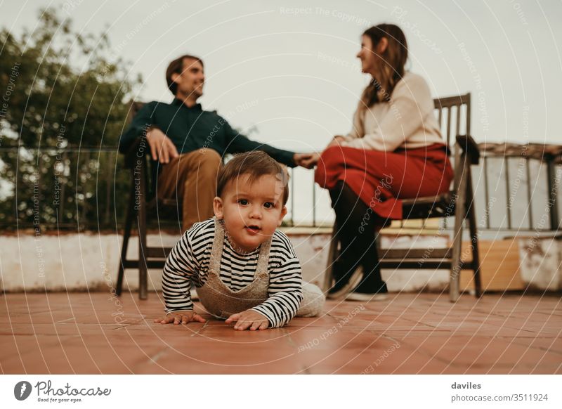 Cute baby infant crawling away from their parents, that are sitting in the background. Baby looks at camera. fatherhood cute eyes house cheerful talking