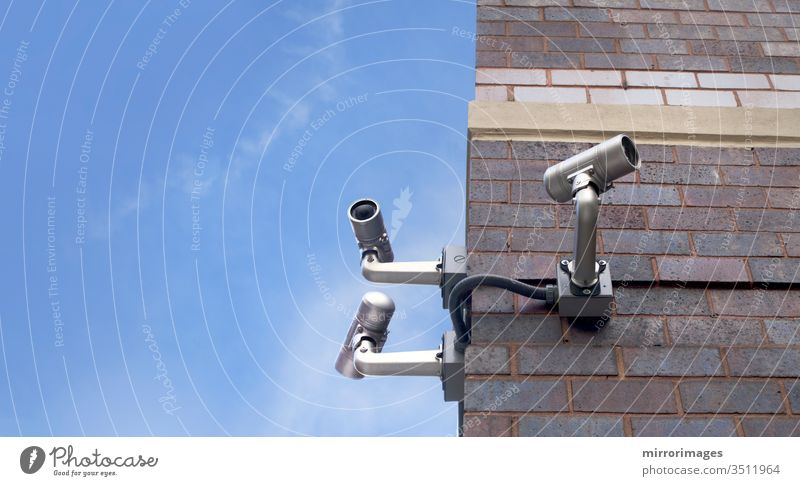 corner of an outdoor brick building with 3 csurveillance camera poiinting in different directions on a beautiful day cctv city control electronic equipment lens