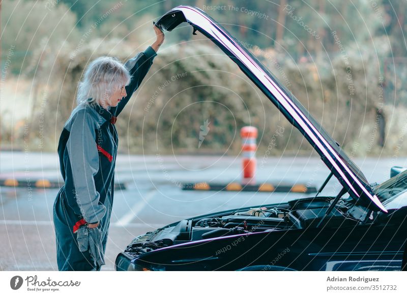 Attractive young blonde female wearing an auto mechanic uniform and repairing the car automobile caucasian vehicle attractive background black blue machine